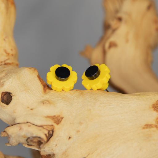 A pair of simple yellow flowers with a black circle center as stud earrings. They are resting on a branch that is resting on a light grey background